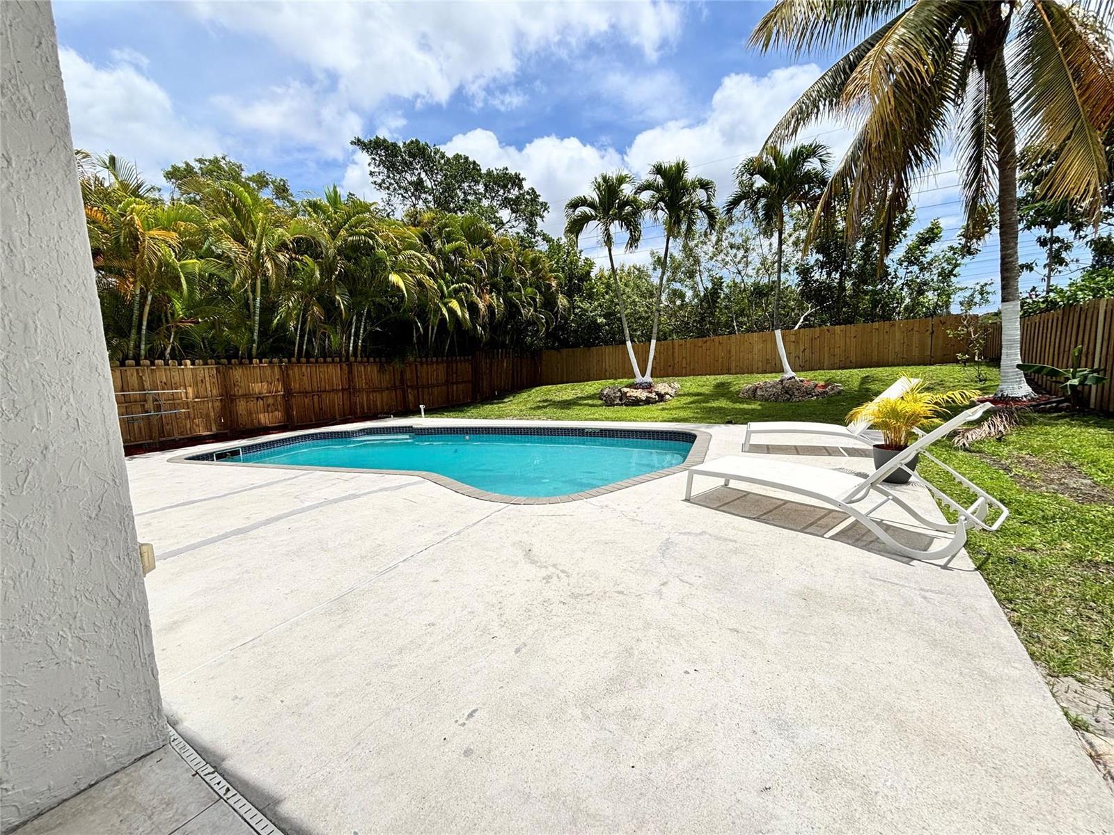 A backyard features a swimming pool, concrete patio, lounge chairs, and palm trees with a fence — 2990 NW 68th Avenue, Margate FL 33063, MARGATE, FL