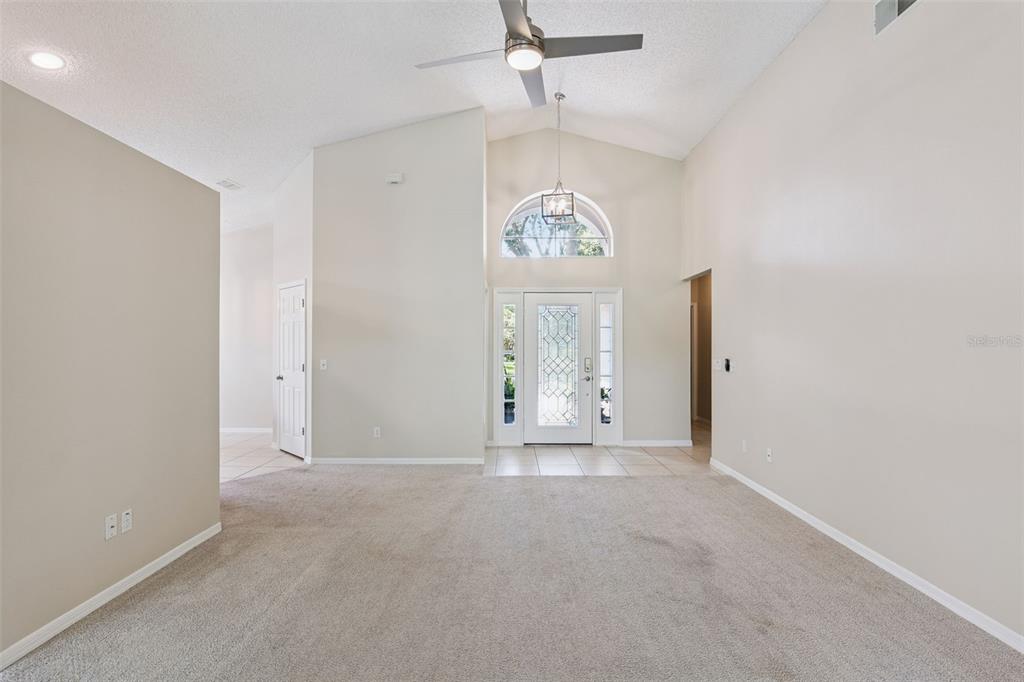 A spacious living room with vaulted ceilings, beige carpeting, and a front entryway with glass — 893 PADDINGTON TERRACE, LAKE MARY, FL