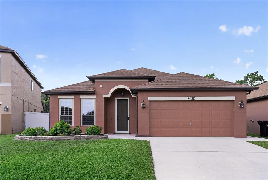 A single-story house with a brown stucco exterior, a two-car garage, and a landscaped yard — 5036 HEARTLAND STREET, ORLANDO, FL