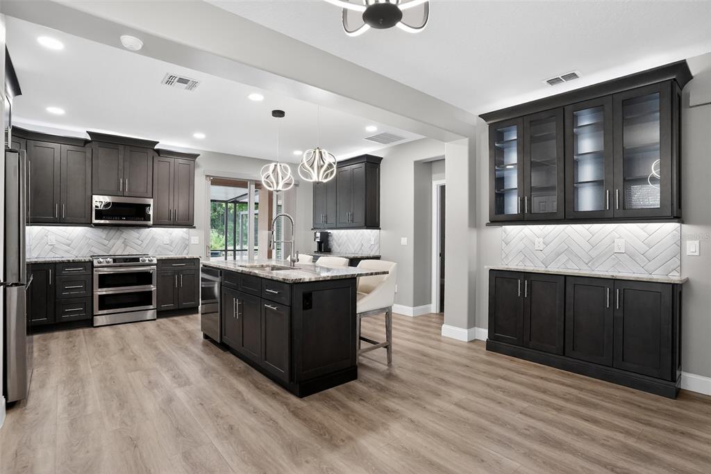 A modern kitchen features dark cabinetry, a central island, stainless steel appliances, and herringbone backsplash — 5036 HEARTLAND STREET, ORLANDO, FL