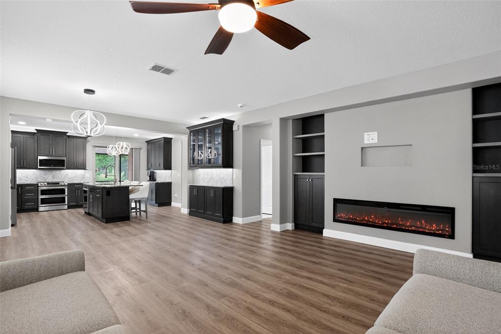 A living room with a linear electric fireplace, built-in shelving, and an open-concept kitchen — 5036 HEARTLAND STREET, ORLANDO, FL