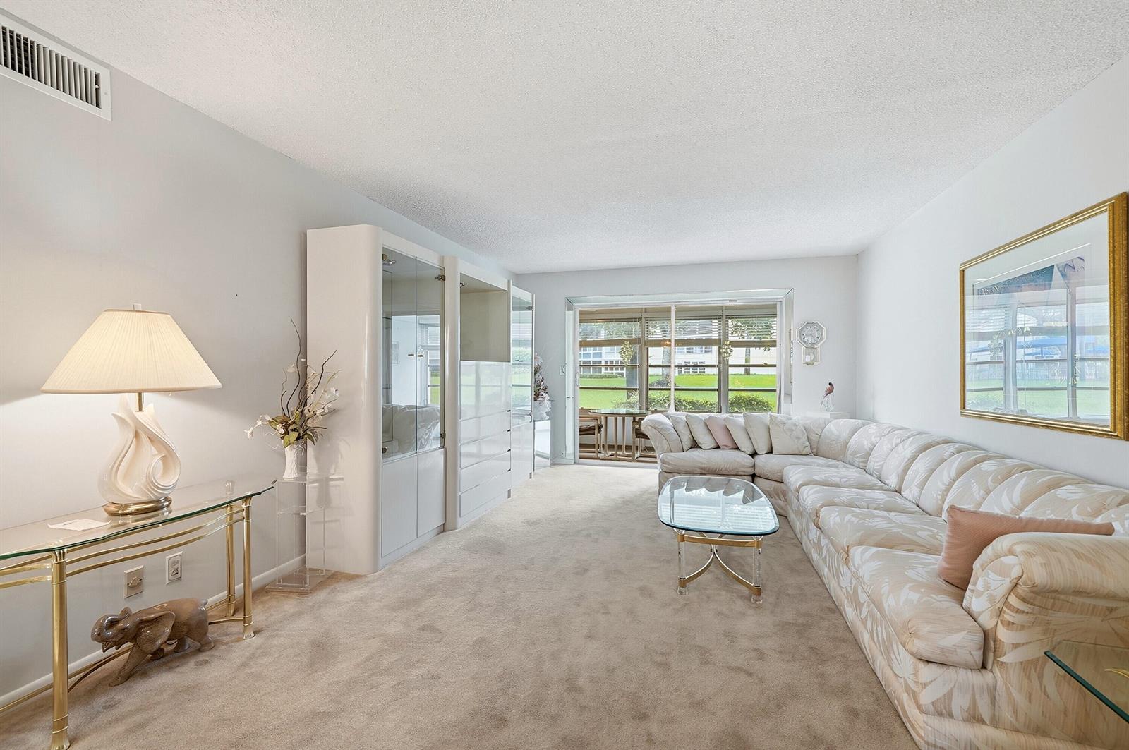 A living room features beige carpeting, a sectional sofa, a glass coffee table, and cabinetry — 2302 Lucaya Lane # E1, Coconut Creek FL 33066, COCONUT CREEK, FL
