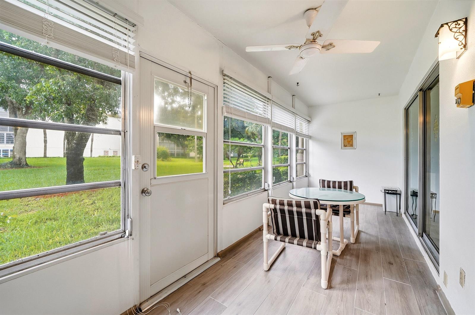 A sunroom with white walls, wood-look tile flooring, a ceiling fan, and a small dining set — 2302 Lucaya Lane # E1, Coconut Creek FL 33066, COCONUT CREEK, FL