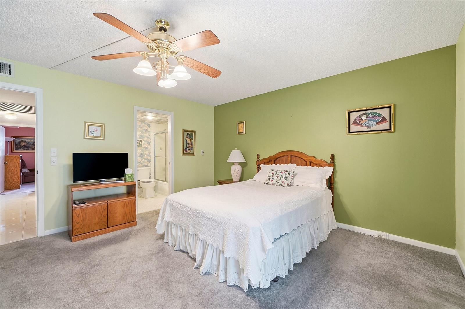 A bedroom with green walls, a white bed, a ceiling fan, and an attached bathroom — 2302 Lucaya Lane # E1, Coconut Creek FL 33066, COCONUT CREEK, FL