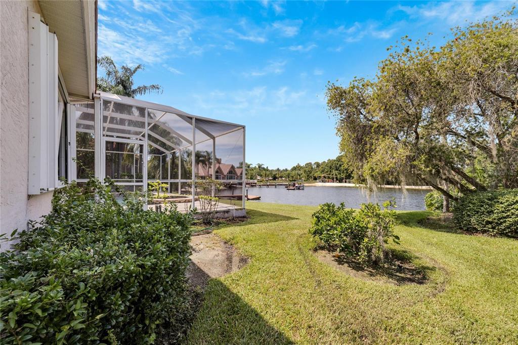 A screened-in pool enclosure sits on a grassy lawn overlooking a lake with docks — 17904 CACHET ISLE DRIVE, TAMPA, FL