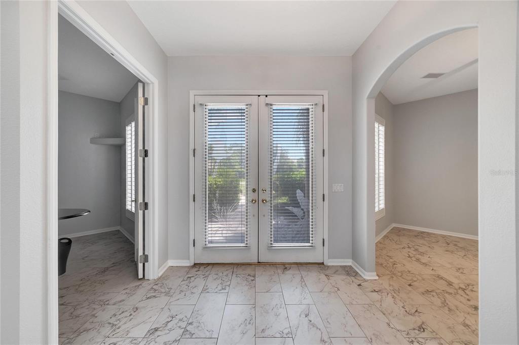 A foyer with marble-look tile flooring, double glass doors, and arched entryways to adjacent rooms — 17904 CACHET ISLE DRIVE, TAMPA, FL