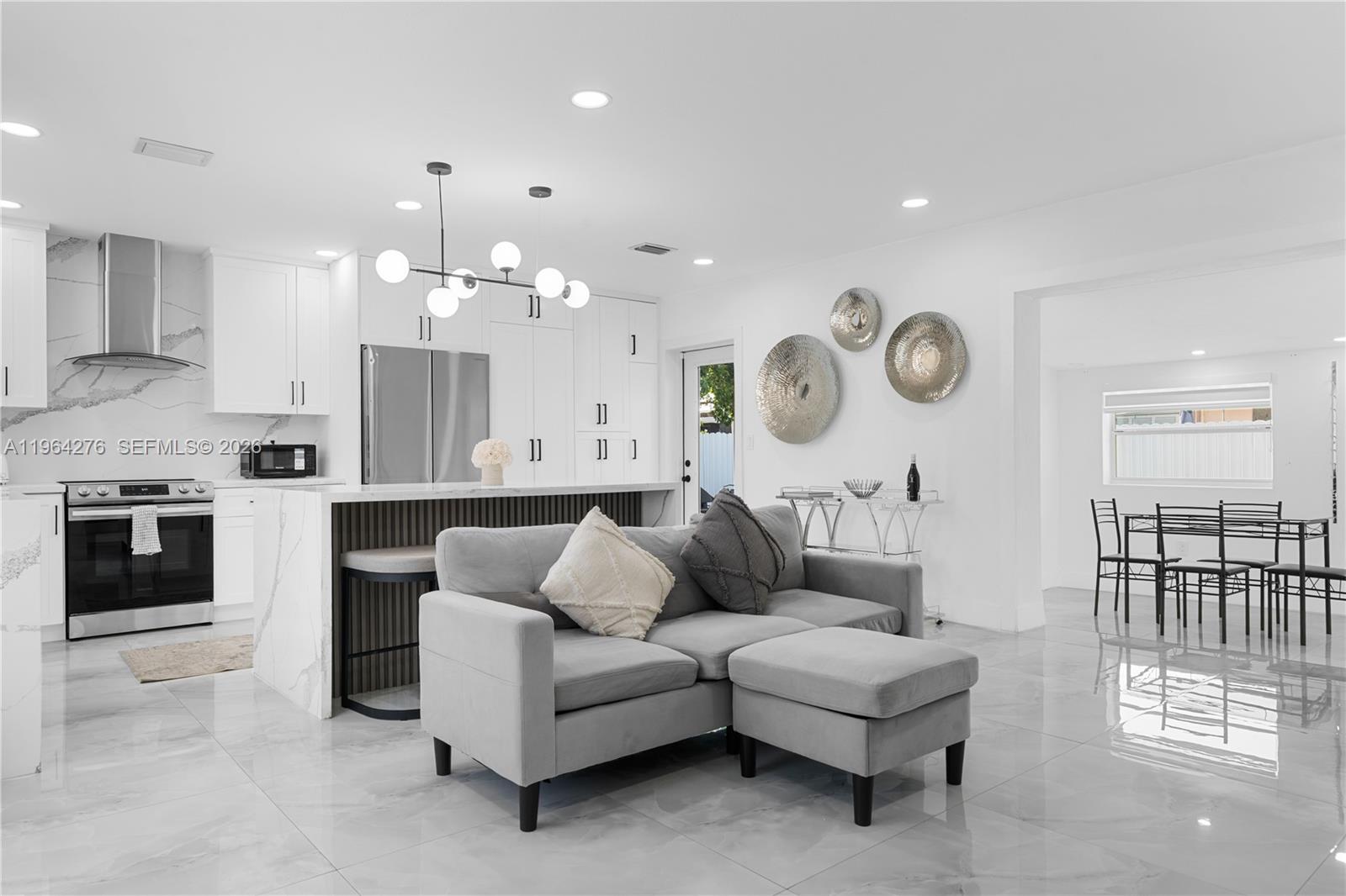 A modern open-concept kitchen and living area features white cabinetry, marble countertops, and gray tile — 315 NW 106th ST, Miami FL 33150, MIAMI, FL