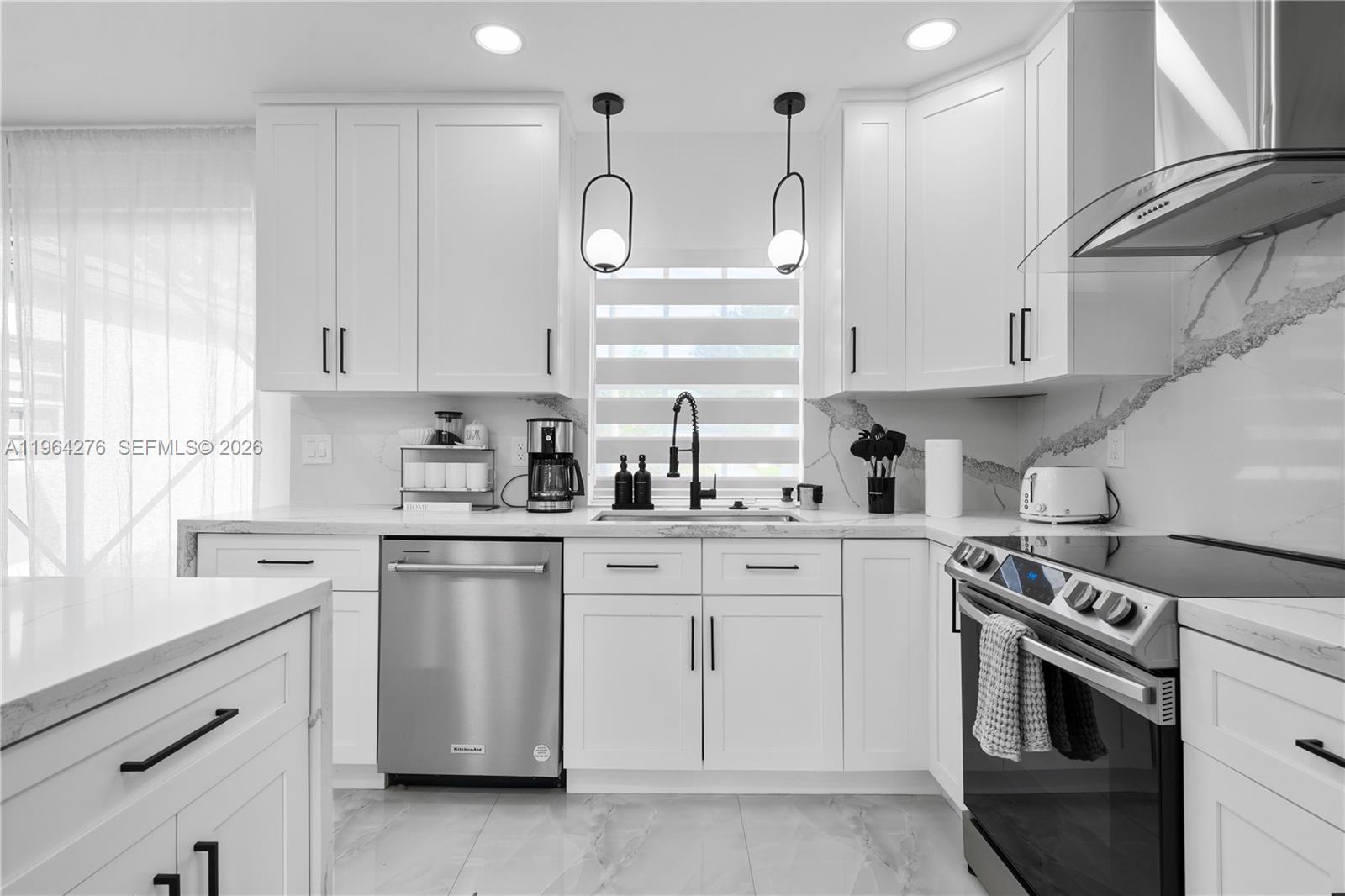 A modern kitchen features white cabinetry, stainless steel appliances, and marble-patterned countertops and backsplash — 315 NW 106th ST, Miami FL 33150, MIAMI, FL