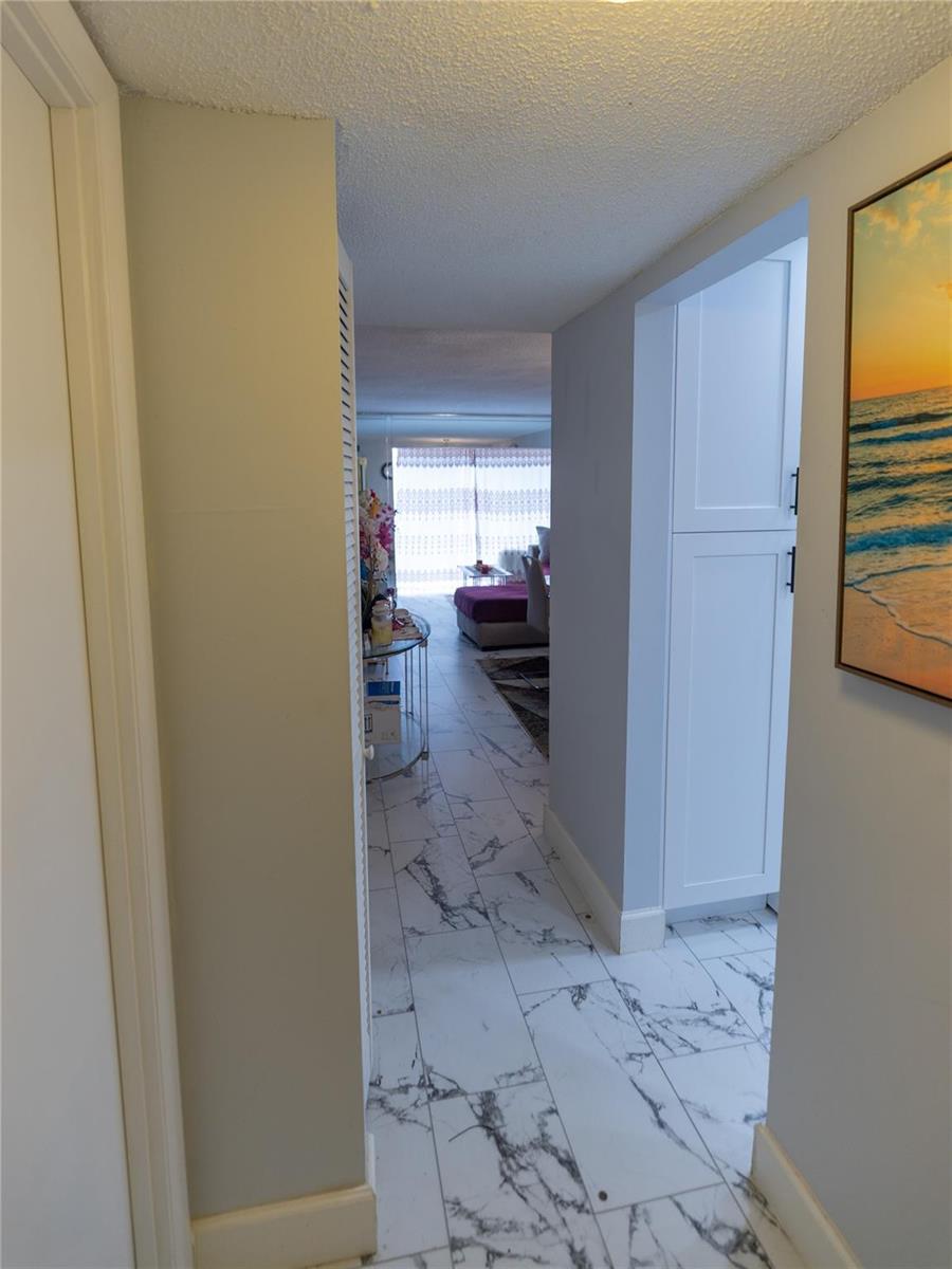 A hallway with white marble-patterned tile flooring leads toward a living area with large windows — 3140 Holiday Springs Boulevard # 210, Margate FL 33063, MARGATE, FL