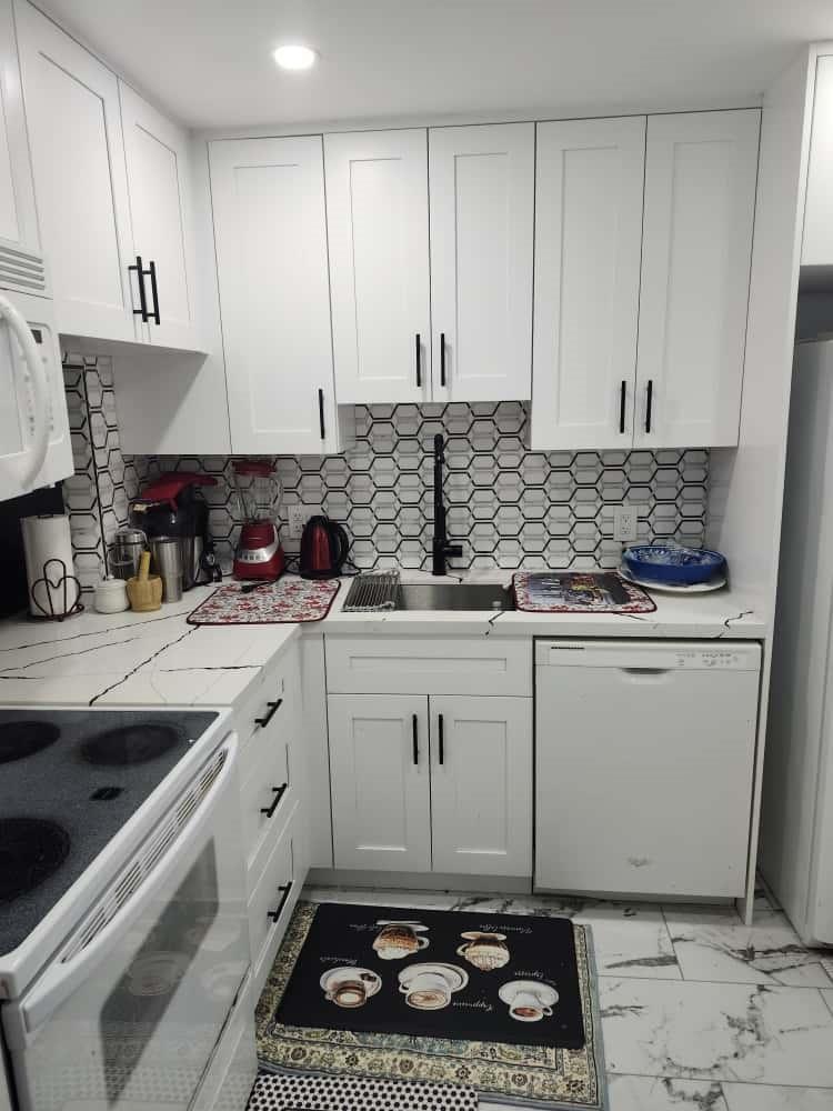 A small kitchen features white shaker cabinets, a black-and-white honeycomb backsplash, and marble-patterned countertops — 3140 Holiday Springs Boulevard # 210, Margate FL 33063, MARGATE, FL