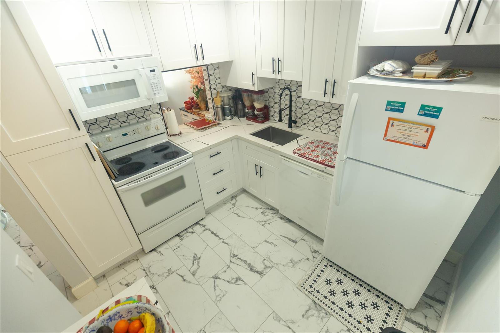 A white kitchen features marble-patterned tile flooring, white cabinetry, and a black-and-white hexagonal backsplash — 3140 Holiday Springs Boulevard # 210, Margate FL 33063, MARGATE, FL