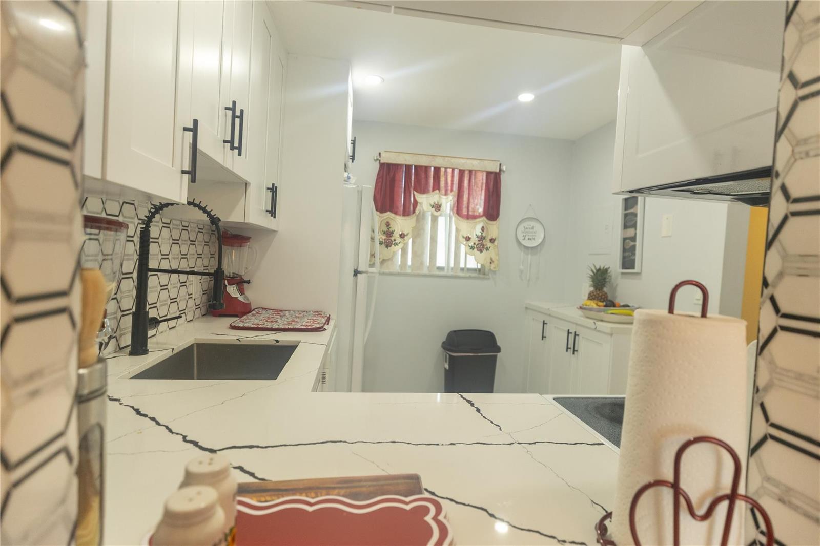 A kitchen features white cabinets, black hardware, a marble-patterned countertop, and a patterned backsplash — 3140 Holiday Springs Boulevard # 210, Margate FL 33063, MARGATE, FL