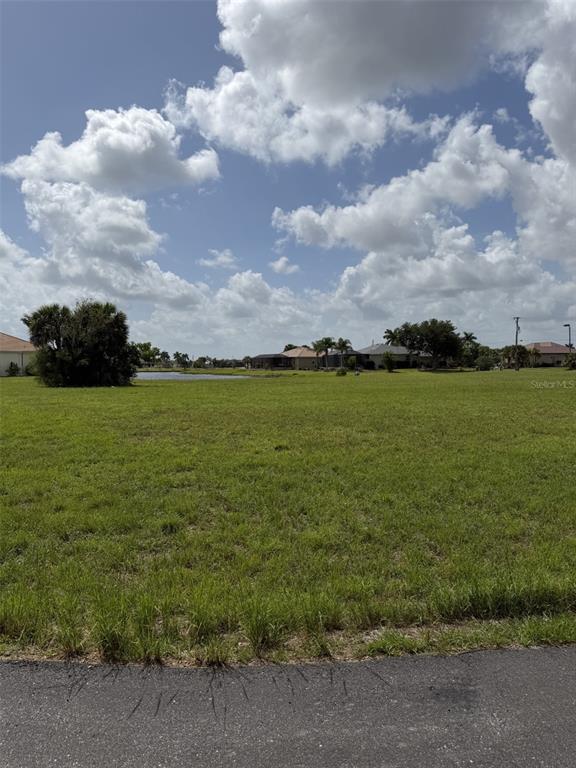 A vacant grassy lot features a small pond and distant houses under a cloudy sky — 15692 SAN EDMUNDO ROAD, PUNTA GORDA, FL