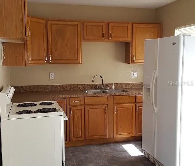 A kitchen features oak cabinets, a white stove, a double-door refrigerator, and a stainless sink — 1235 MORGAN DRIVE, LAKELAND, FL