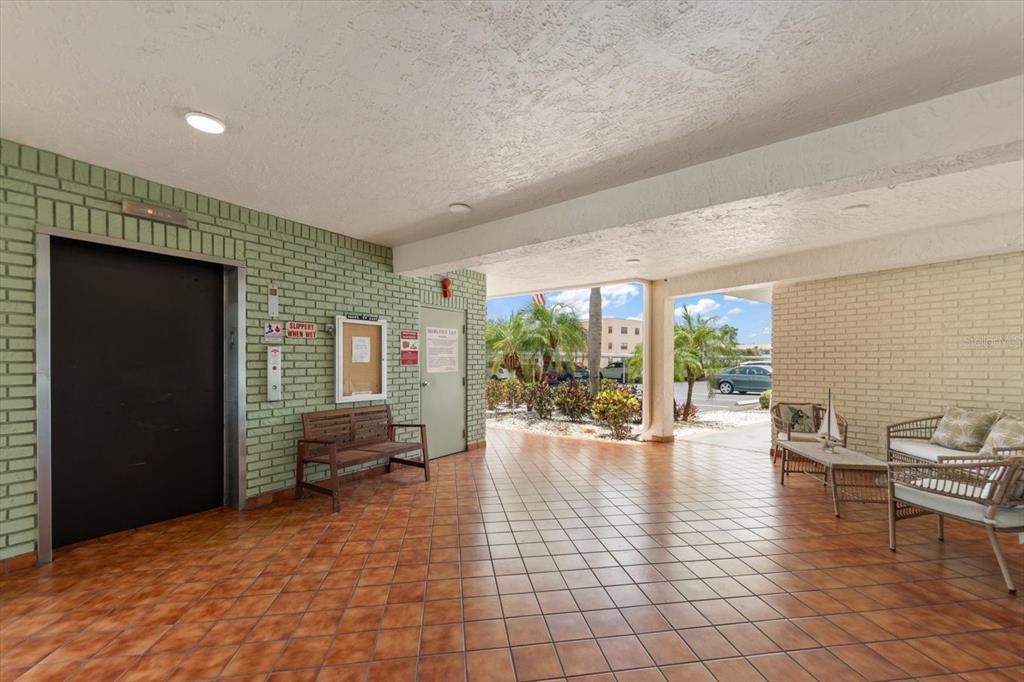 An open-air lobby features tiled floors, a brick wall, an elevator, and outdoor seating — 5980 TERRACE PARK DRIVE N UNIT 310, ST PETERSBURG, FL