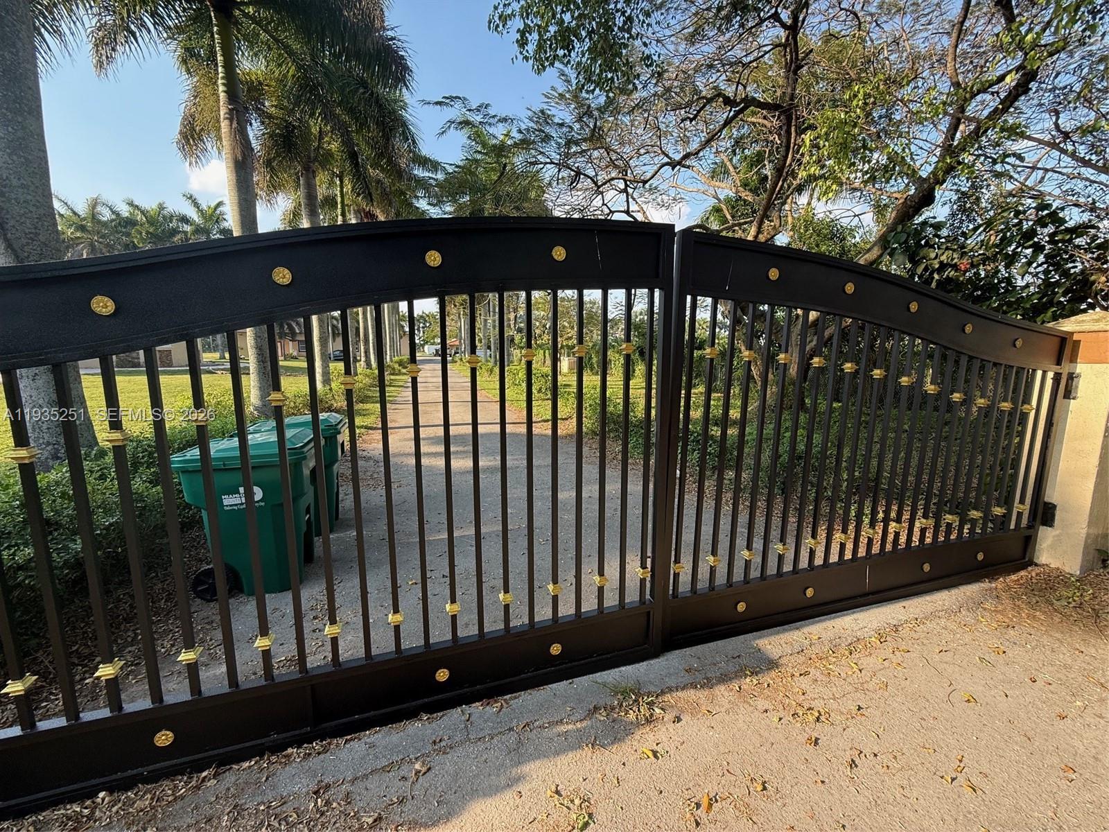 A black metal driveway gate with gold accents stands at the entrance of a property — 19701 SW 197th Ave, Miami FL 33187, MIAMI, FL