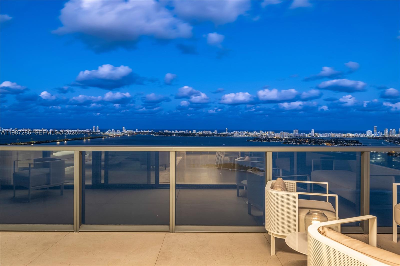 A balcony with modern white chairs overlooks a city skyline across a body of water — 788 NE 23rd St # 3801, Miami FL 33137, MIAMI, FL