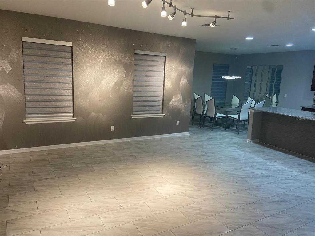 A living room with a metallic textured wall, tile flooring, and an adjacent dining area — 2618 SAN SIMEON WAY, KISSIMMEE, FL