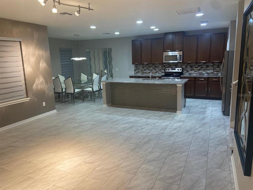 A kitchen with dark wood cabinets, a granite island, and tile flooring next to a dining area — 2618 SAN SIMEON WAY, KISSIMMEE, FL