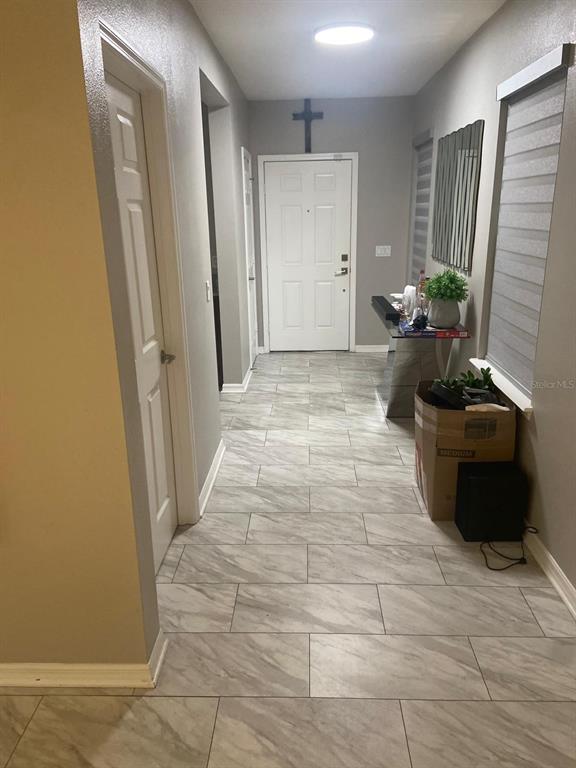 A hallway with light gray marble-look tile flooring leads to a white front door — 2618 SAN SIMEON WAY, KISSIMMEE, FL