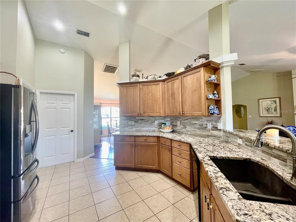A kitchen features wood cabinets, granite countertops, a tiled backsplash, and light-colored floor tiles — 5525 SW 89TH PLACE, OCALA, FL