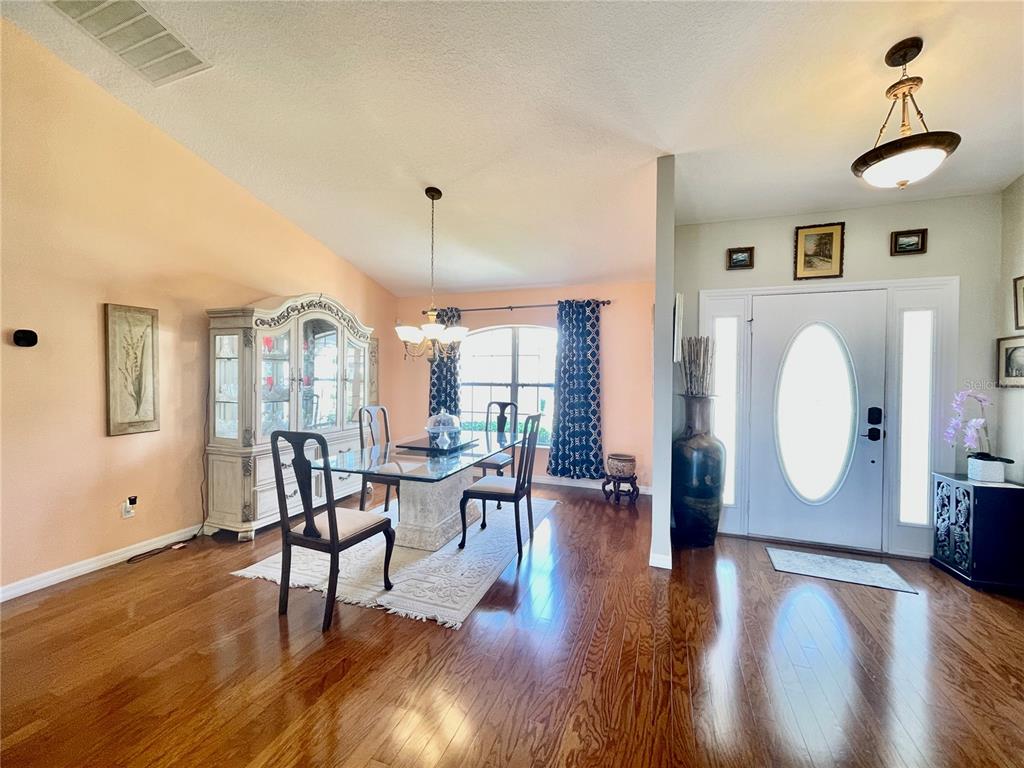A dining room with hardwood floors, a glass table, and a white front door entrance — 5525 SW 89TH PLACE, OCALA, FL