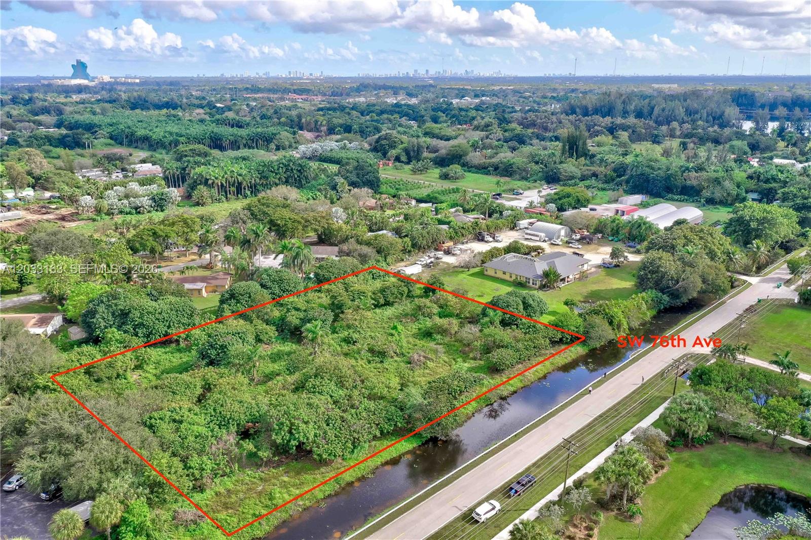 An aerial view shows a rectangular, tree-covered vacant lot adjacent to a road and canal — 76 SW Ave, Davie FL 33314, DAVIE, FL