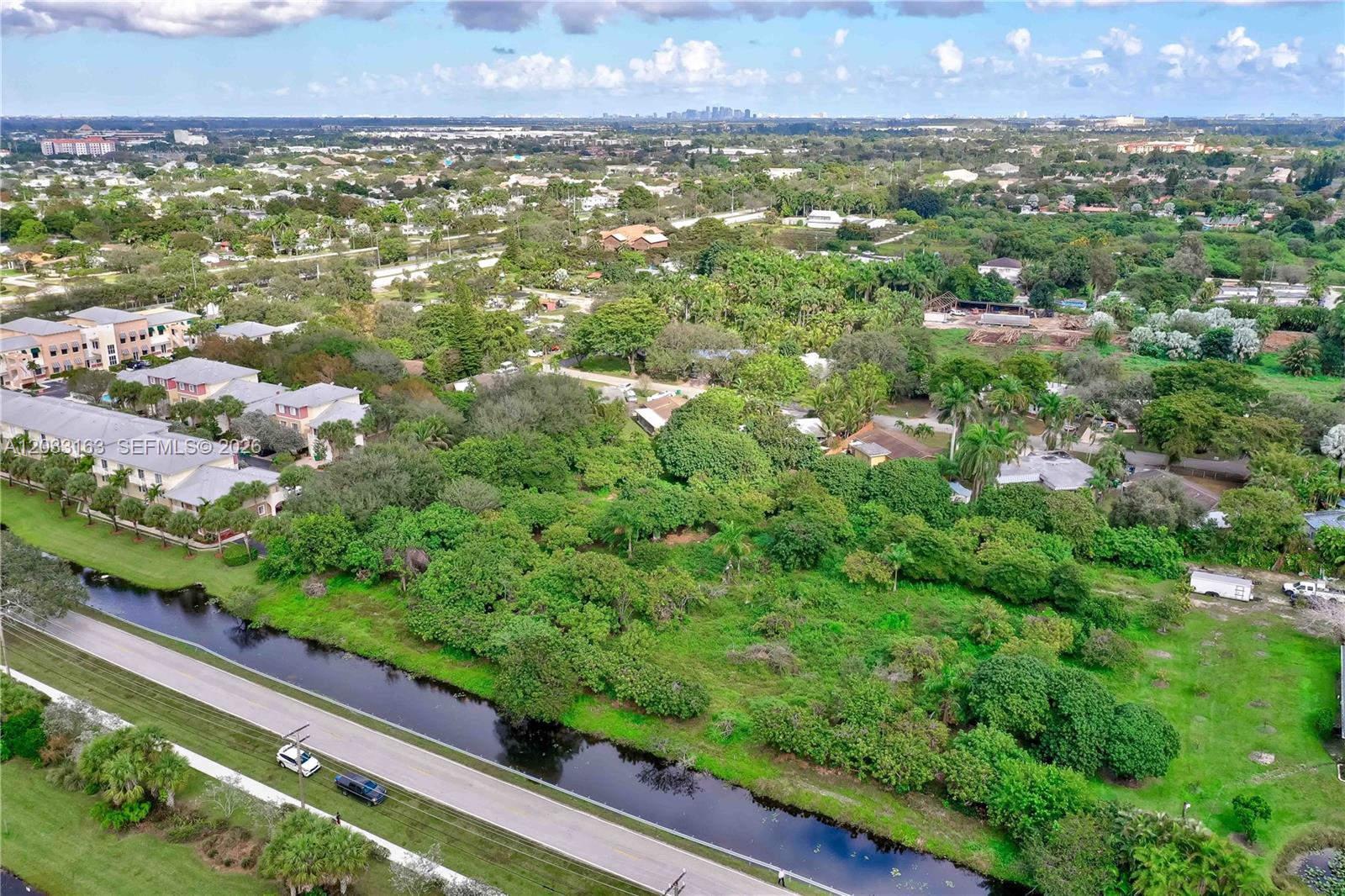 An aerial view shows a vacant, tree-covered lot adjacent to a canal and residential buildings — 76 SW Ave, Davie FL 33314, DAVIE, FL