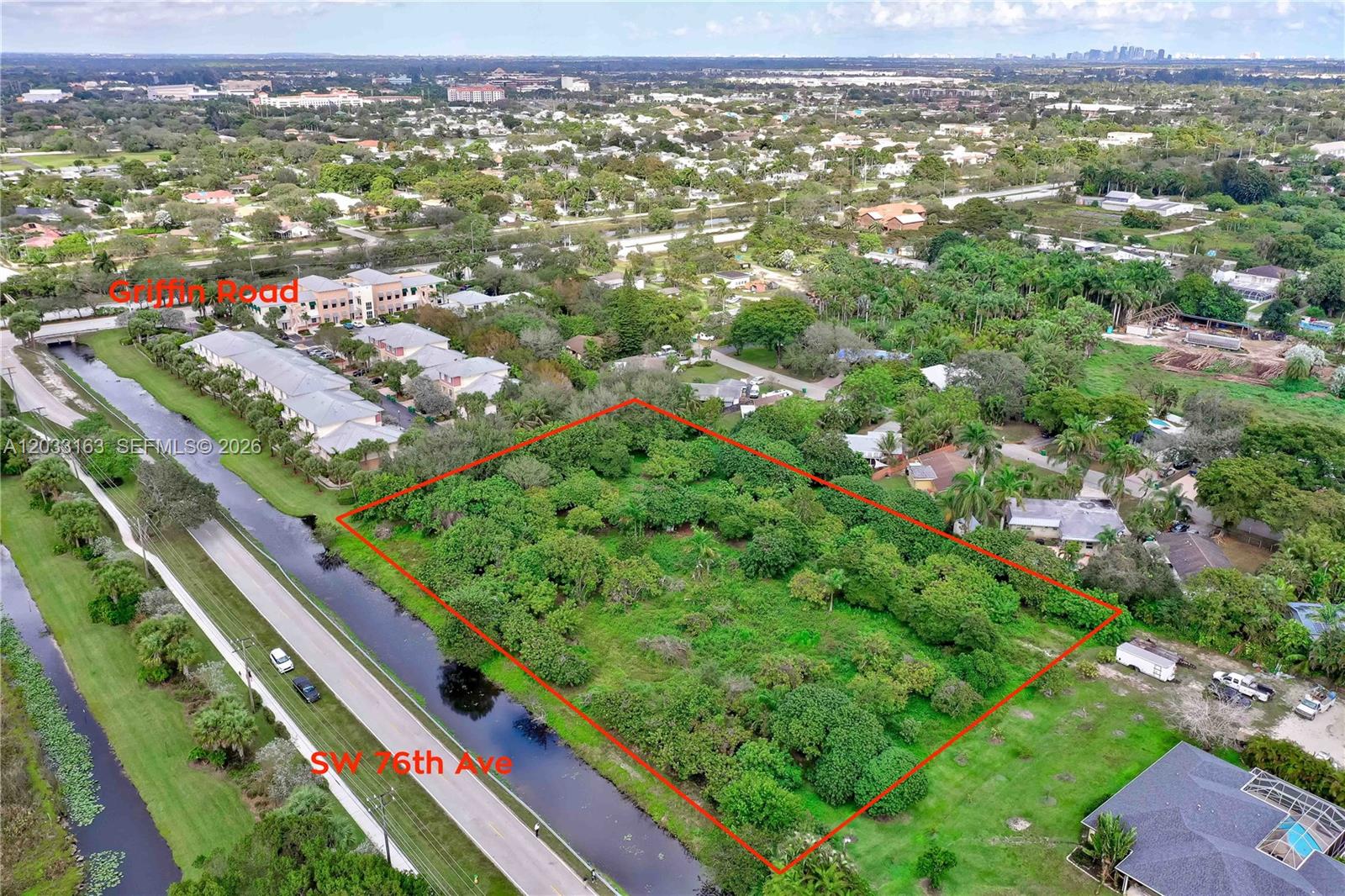 An aerial view shows a rectangular, tree-covered vacant lot bordered by a road and canal — 76 SW Ave, Davie FL 33314, DAVIE, FL