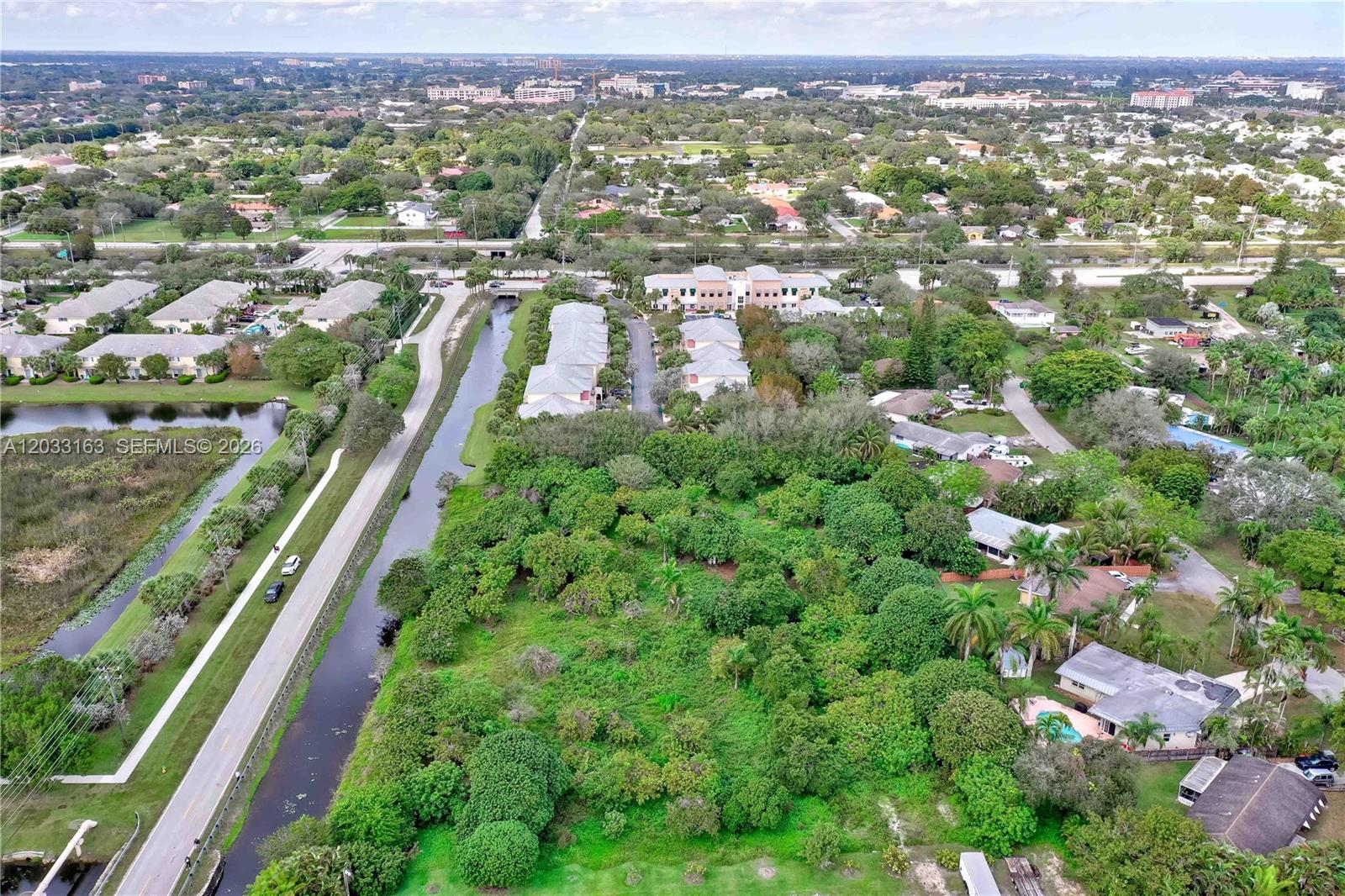 An aerial view shows a residential area with a canal, dense trees, and nearby buildings — 76 SW Ave, Davie FL 33314, DAVIE, FL