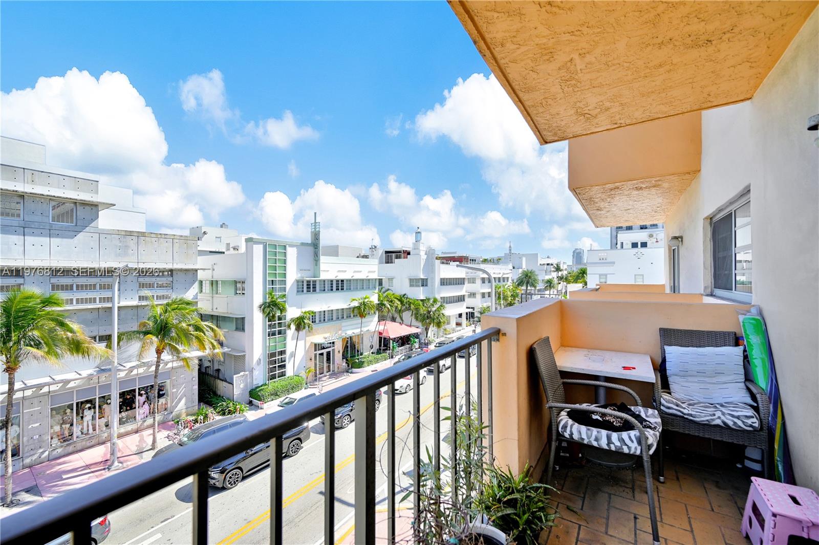 A balcony with outdoor furniture overlooks a street lined with Art Deco buildings — 1150 Collins Ave # 405, Miami Beach FL 33139, MIAMI BEACH, FL