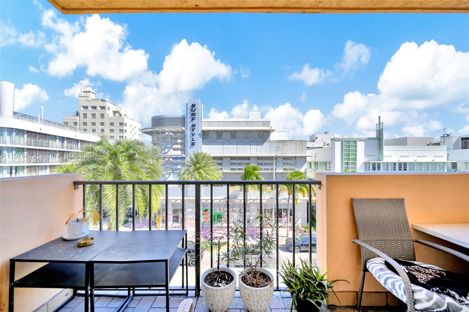 A balcony with a black metal table, chairs, and potted plants overlooks a city street — 1150 Collins Ave # 405, Miami Beach FL 33139, MIAMI BEACH, FL