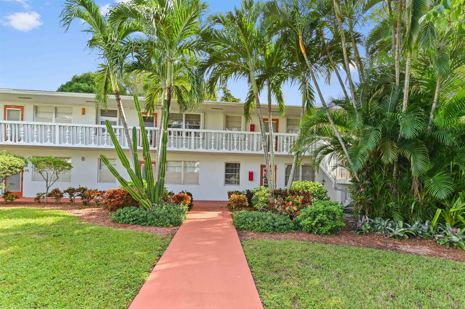 A two-story apartment building with a white exterior, orange doors, and a central walkway — 203 Ellesmere D, Deerfield Beach FL 33442, DEERFIELD BEACH, FL