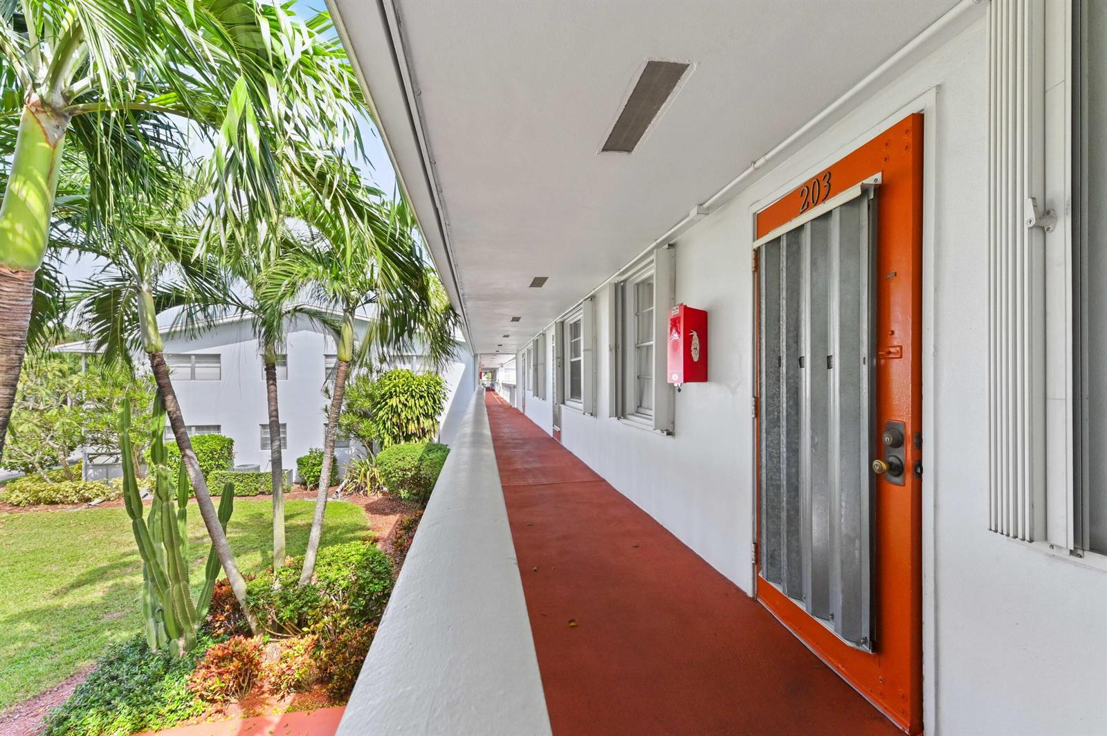 An exterior walkway with a red floor leads past an orange door labeled 203 — 203 Ellesmere D, Deerfield Beach FL 33442, DEERFIELD BEACH, FL