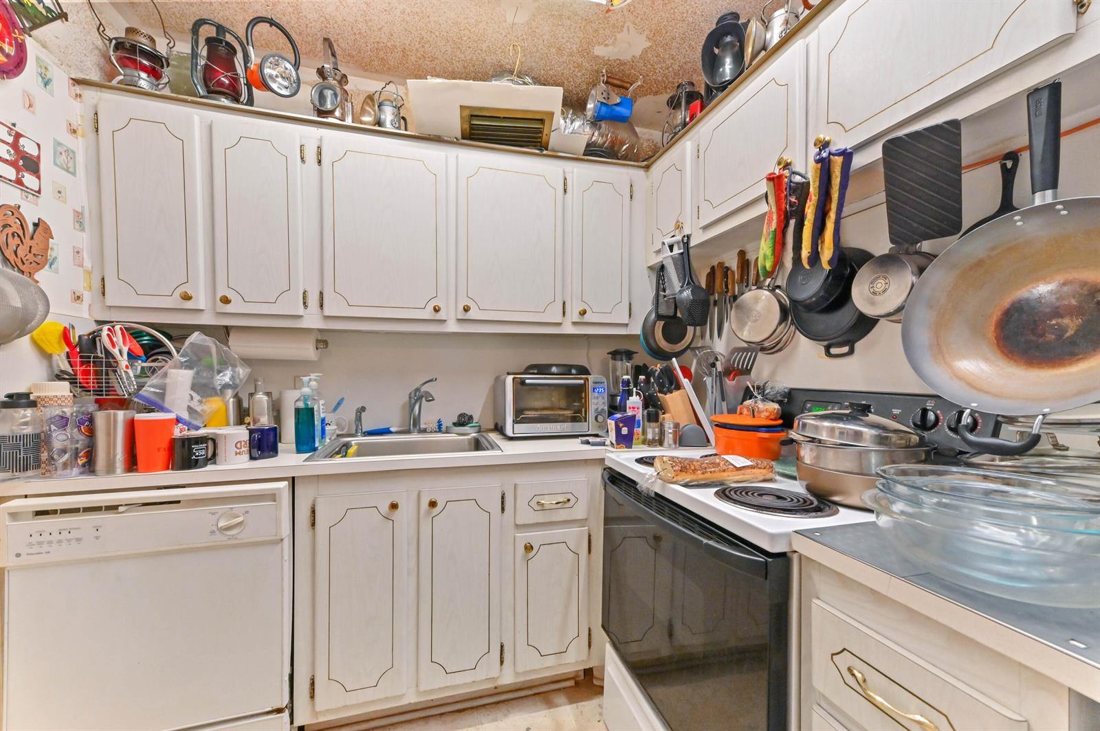 A cluttered kitchen features white cabinets, a stainless steel sink, and a black electric stove — 203 Ellesmere D, Deerfield Beach FL 33442, DEERFIELD BEACH, FL