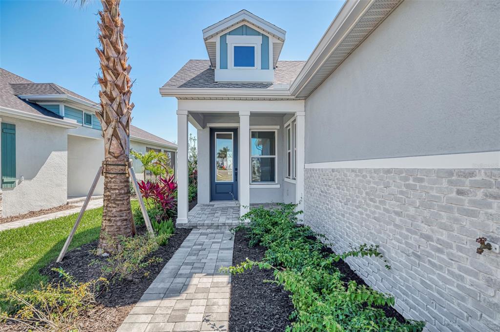 A paved walkway leads to the front entrance of a house with gray brick siding — 2821 MARRAKESH LANE, SARASOTA, FL