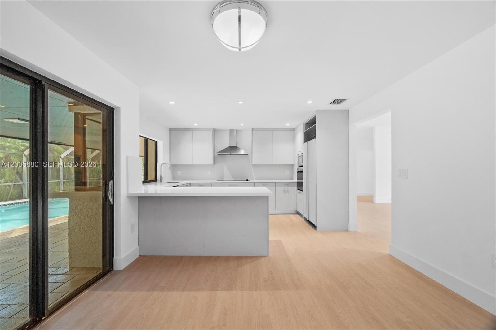 A modern kitchen features white cabinetry, a peninsula, and light wood flooring — 5254 NW 94th Doral Pl, Doral FL 33178, DORAL, FL