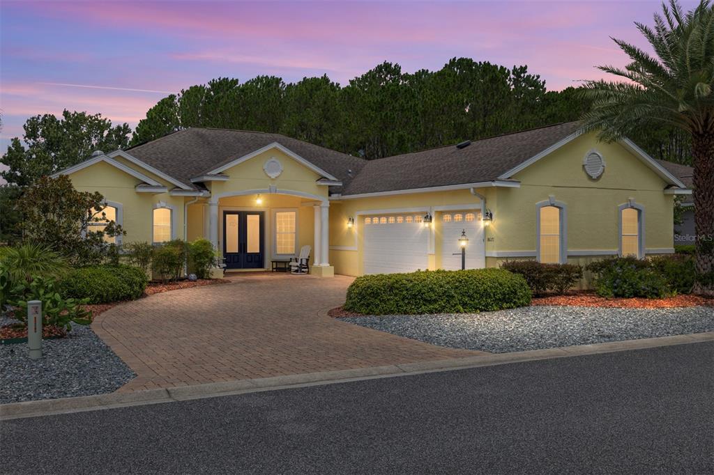A yellow single-story house with a brick driveway and a two-car garage at dusk — 8671 SW 83RD LOOP, OCALA, FL