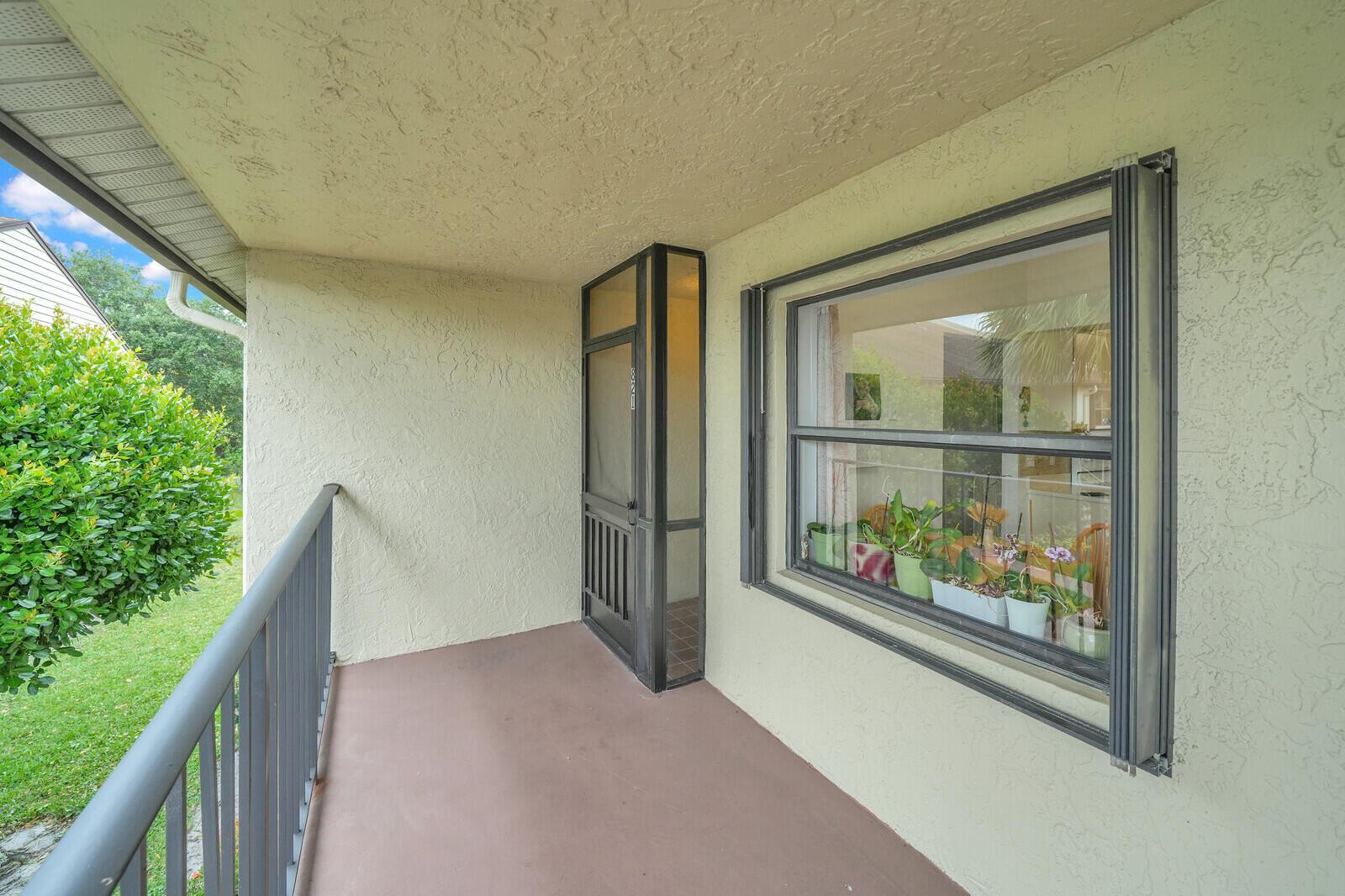 A covered balcony features a metal railing, a screen door, and a large window with plants — 7867 Willow Spring Drive # 821, Lake Worth FL 33467, LAKE WORTH, FL