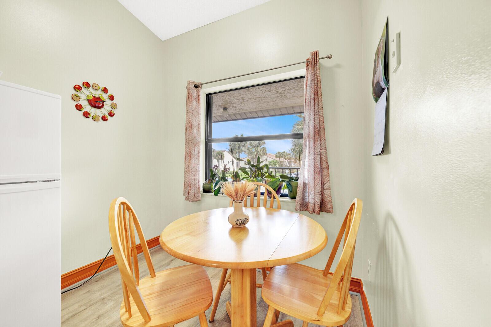 A dining nook features a round wooden table, three chairs, and a window with curtains — 7867 Willow Spring Drive # 821, Lake Worth FL 33467, LAKE WORTH, FL