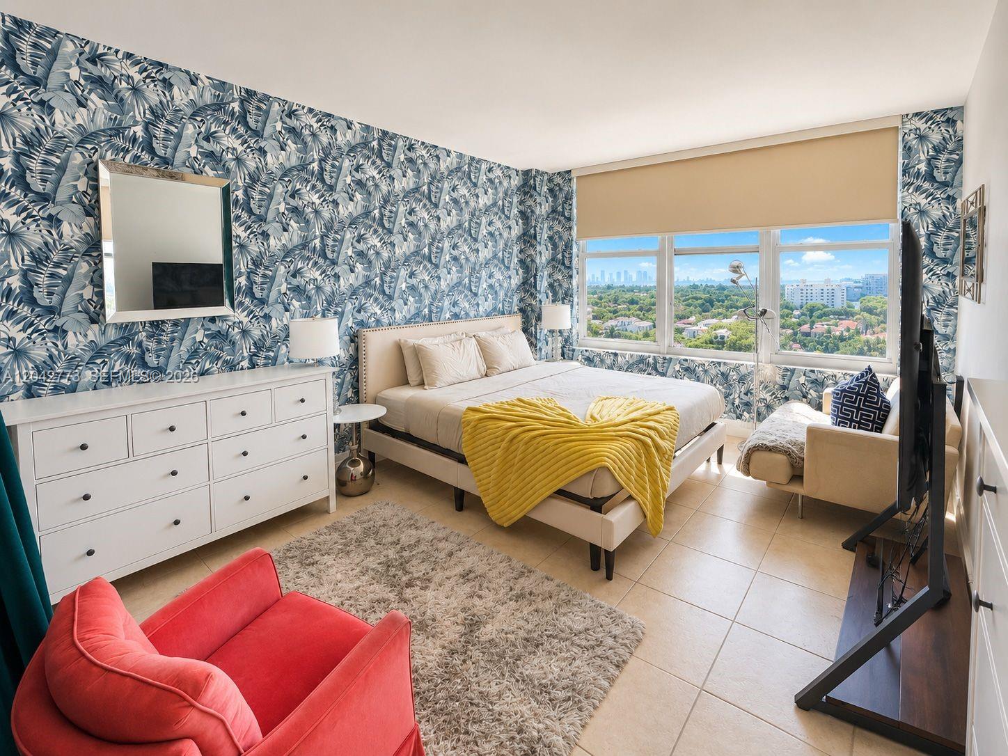 A bedroom features blue tropical wallpaper, a white dresser, a bed with yellow bedding, and windows — 4747 Collins Ave # 1101, Miami Beach FL 33140, MIAMI BEACH, FL