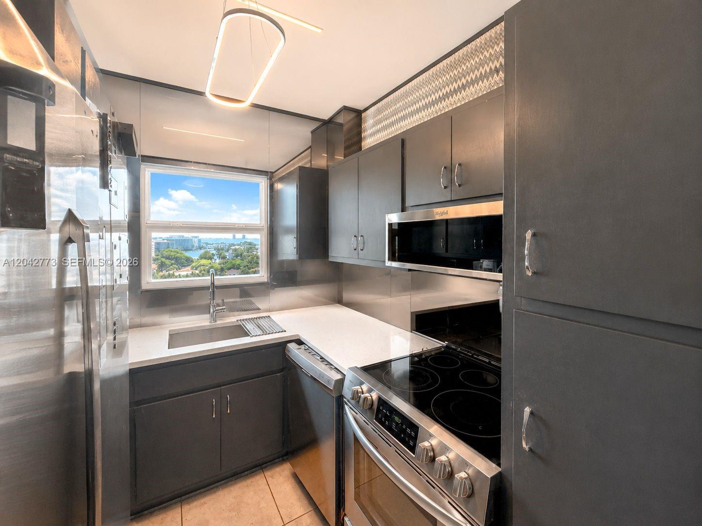 A modern galley kitchen features dark cabinetry, stainless steel appliances, and a window with views — 4747 Collins Ave # 1101, Miami Beach FL 33140, MIAMI BEACH, FL