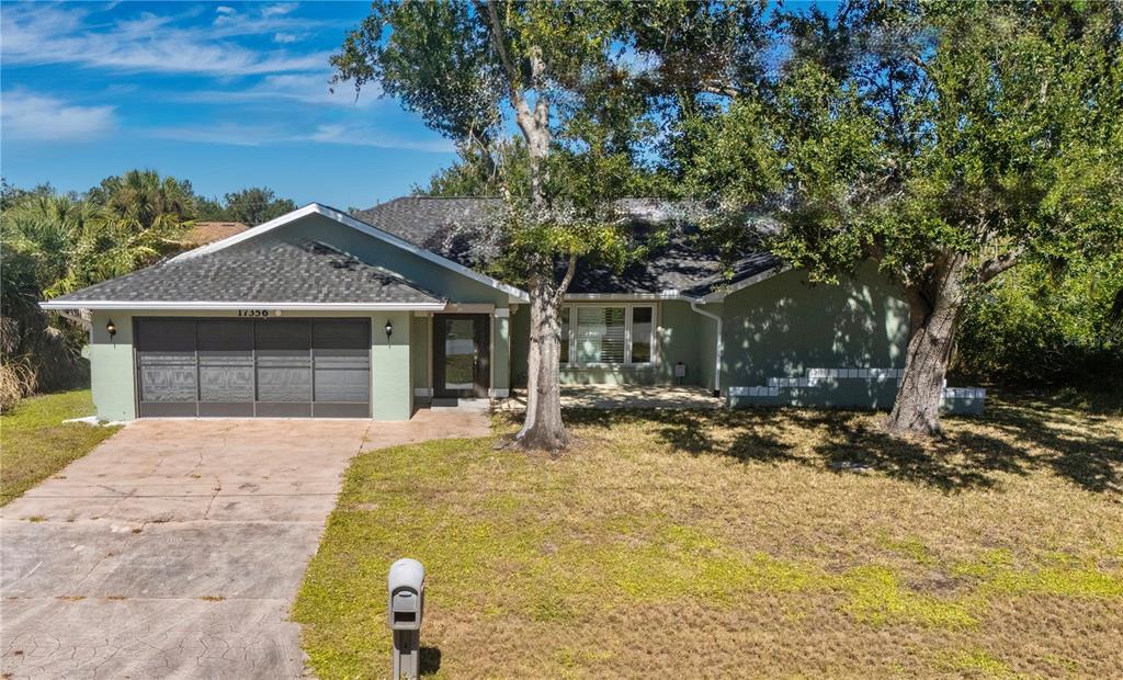 A single-story house with a green exterior, a two-car garage, and a large front tree — 17356 GULFSPRAY CIRCLE, PORT CHARLOTTE, FL