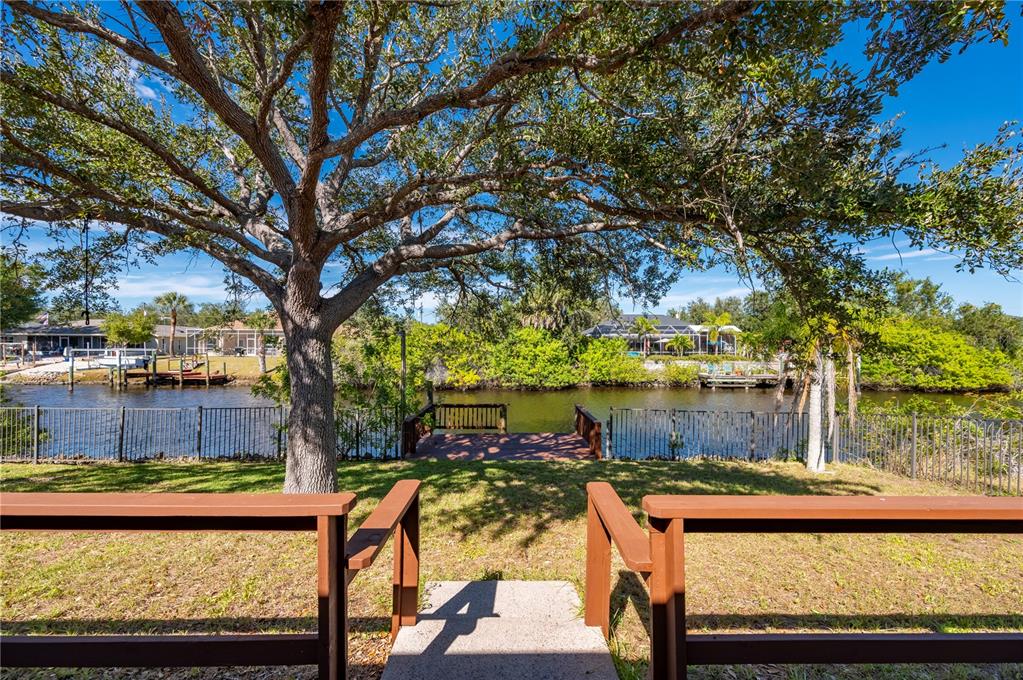 A backyard view features a wooden deck, a metal fence, and a canal with trees — 17356 GULFSPRAY CIRCLE, PORT CHARLOTTE, FL