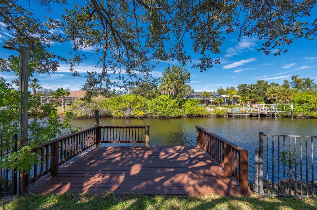 A wooden dock with railings overlooks a narrow canal lined with trees and houses — 17356 GULFSPRAY CIRCLE, PORT CHARLOTTE, FL