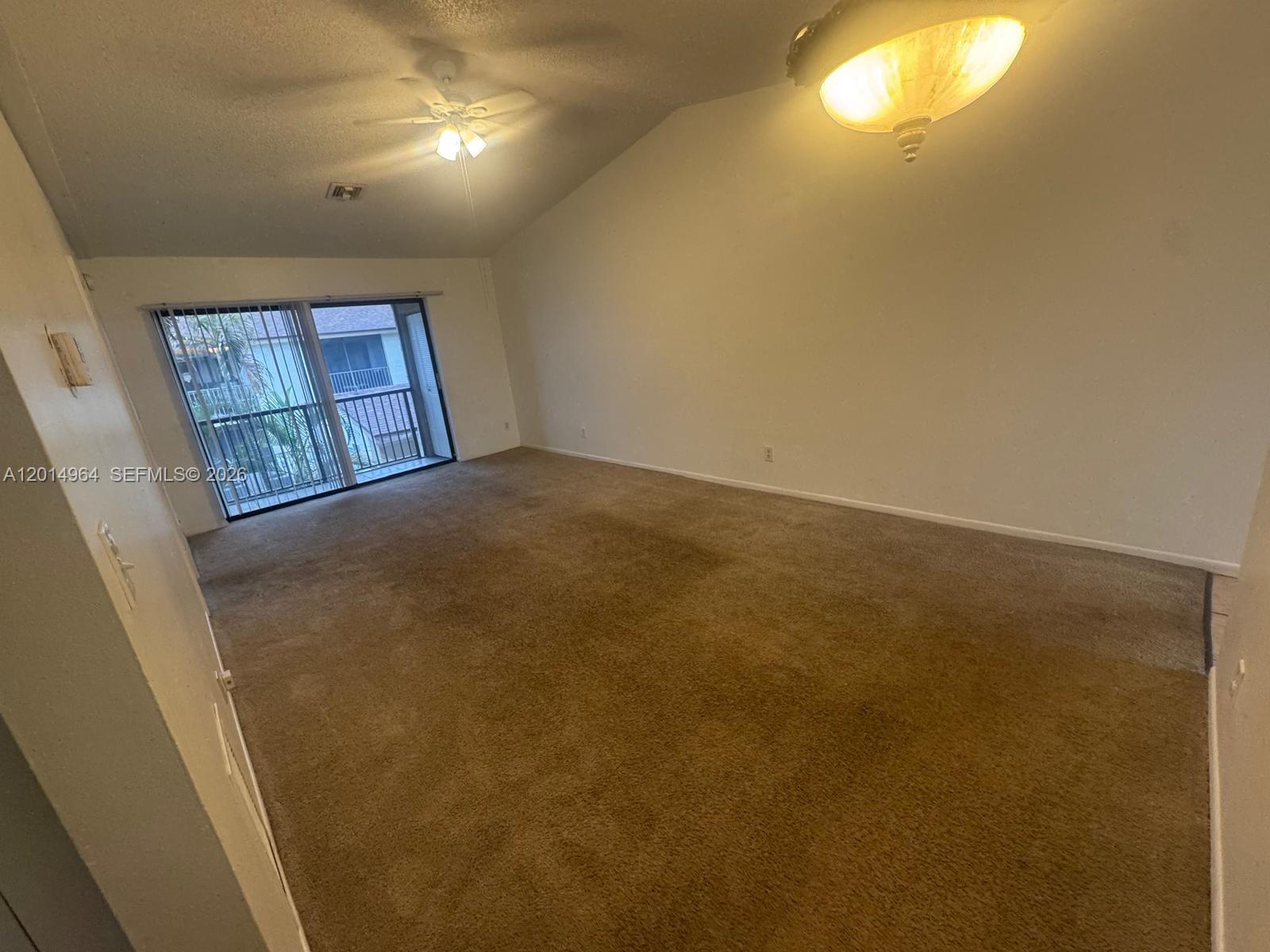 An empty living room features beige carpeting, a vaulted ceiling, and a sliding glass door — 142 NW 60th Ave # 2, Margate FL 33063, MARGATE, FL