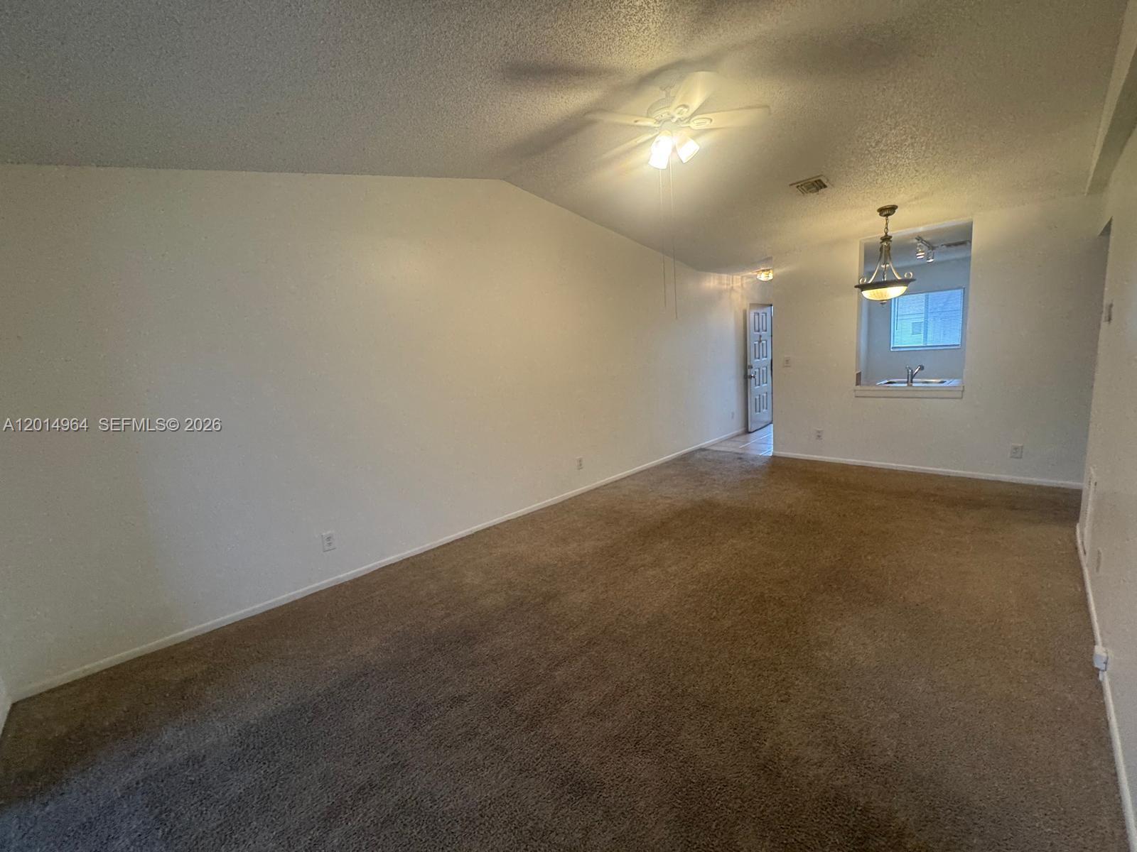 A carpeted living room with a vaulted ceiling, ceiling fan, and an adjacent kitchen pass-through — 142 NW 60th Ave # 2, Margate FL 33063, MARGATE, FL
