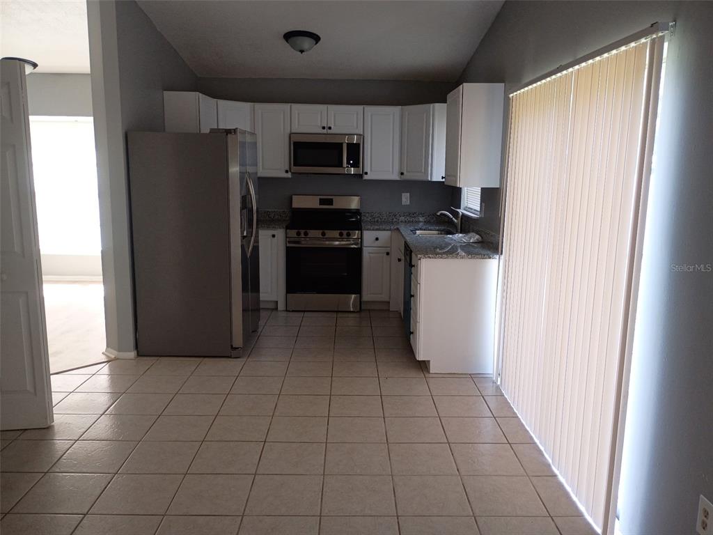 A kitchen features white cabinets, stainless steel appliances, granite countertops, and light-colored tile flooring — 1359 PRIMROSE COURT, LAKELAND, FL