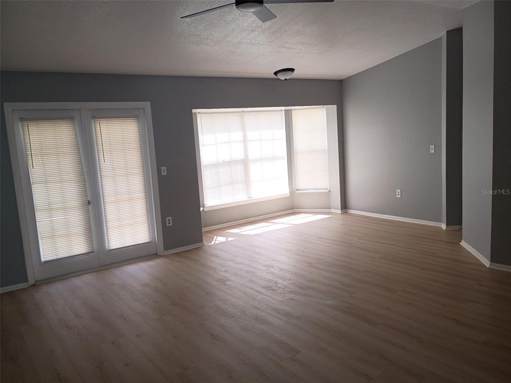 An empty living room features light wood-look flooring, gray walls, a ceiling fan, and French doors — 1359 PRIMROSE COURT, LAKELAND, FL