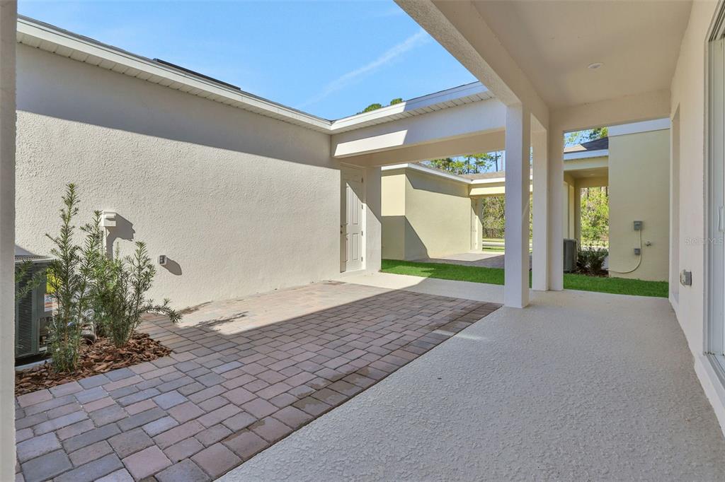 A paved patio area sits beneath a covered walkway connecting two sections of a house — 13011 TRANQUIL WATER ALLEY, WINTER GARDEN, FL